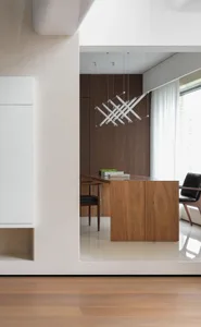 Cozy living space with a wooden cabinet, a refrigerator, two chairs, a dining table, and books, creating a warm and inviting atmosphere