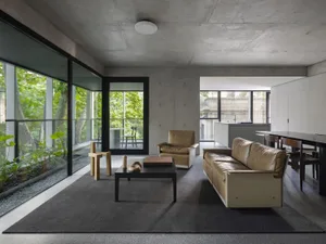 Open modern living area with a couch, chairs, dining tables, and a potted plant, creating a spacious and inviting atmosphere