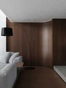 Cozy living area with a couch, chair, and lamp, surrounded by wooden panel walls and illuminated by a prominent lamp