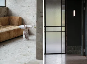 Modern living space with a leather sofa in front of a sink-equipped wall, and a glass door leading to an exterior view with windows