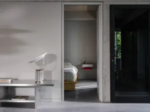 A calm bedroom with two beds and a chair, featuring a double bed near the door and a smaller bed further back, with a chair nearby