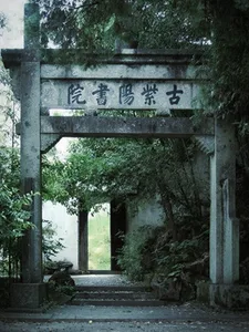 A serene Asian-style entrance with a stone archway featuring Chinese characters, surrounded by trees in a peaceful courtyard