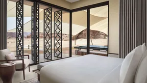 A hotel bedroom with a white-covered bed, two chairs, and a dining table, creating a calm and inviting atmosphere