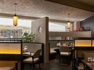 A restaurant dining area with tables, chairs, and potted plants, lit with warm and inviting lighting