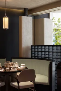A modern dining area with a black color scheme, featuring a table and chairs, cups, bowls, and spoons, in a restaurant-like setting