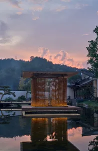 A serene Asian-style building with a wooden structure and large wooden roof, overlooking a pond with a balcony, in a traditional and harmonious style with earth tones and warm lighting