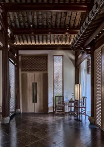 Asian-style interior design with wooden floors and walls, featuring a large wooden door, two chairs, and a vase on a surface near the right wall, creating a calm and inviting atmosphere