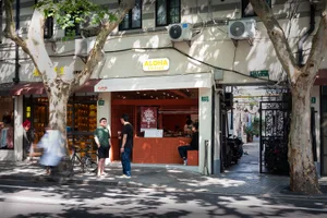 A lively street corner coffee shop with a red door, surrounded by people and bicycles