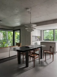 A modern kitchen and dining area with a wooden table, chairs, and a clean minimalist design featuring white walls and grey floors