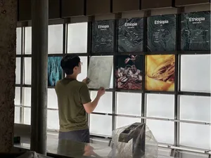 A man works on a poster among a collection of artistic posters on a wall, creating a space that inspires creativity and focus