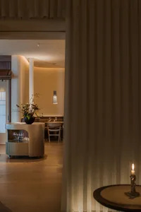 Warm and inviting restaurant interior with wooden floors and walls, featuring dining tables, chairs, wine glasses, and potted plants