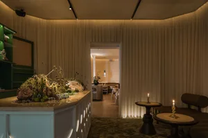 Warm and inviting restaurant interior with a large dining table, potted plants, white walls, and wooden floors