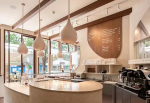 A modern restaurant interior with a counter featuring cups, bottles, and donuts, surrounded by chalkboard signs and a dining table in the background
