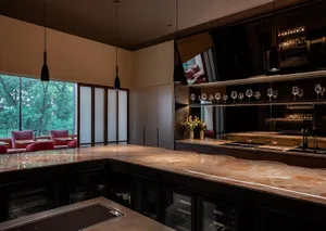 Modern kitchen with a large island, marble countertops, wine glasses, and multiple bottles, featuring a sophisticated design with a focus on functionality and aesthetics