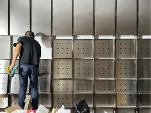 A man works on a metal panel with numerous holes in an industrial setting, with a focus on precision and craftsmanship