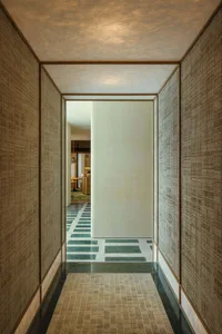 A well-lit hallway with a white wall and brown tiles, featuring two doors and a bright atmosphere