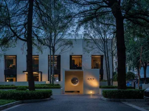 A modern building with a white concrete exterior and a large circular window, surrounded by trees