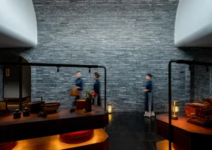 Three women walk through a traditional Chinese interior space with brick walls, potted plants, and decorative vases