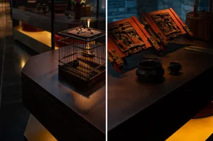 A wooden table in a study space or living area with books, bowls, cups, vases, and a bird cage, suggesting an organized yet casual atmosphere