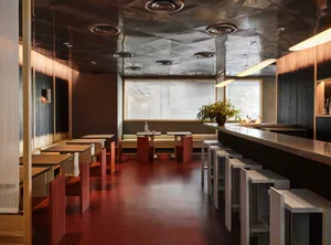 A modern restaurant or bar with a long counter and stools, dining tables, and red tile flooring