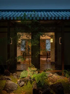 Asian-style house with a tile roof, two doors, potted plants, and chairs in a courtyard