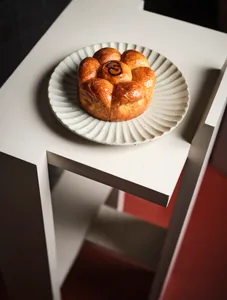 A single croissant on a white plate sits on a simple wooden table in a calm and inviting atmosphere