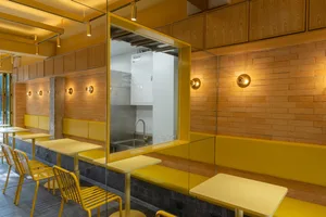 Warm and inviting restaurant interior with yellow walls, tables, chairs, and kitchen appliances
