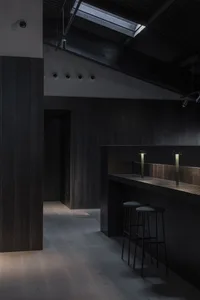 深色調廚房空間，木質牆面與地板，木質料理檯前擺放兩張凳子
