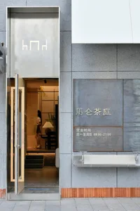現代飯店入口採用灰白配色，擺放盆栽，兩位女性站在通往空蕩走廊的大型入口門前
