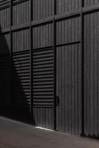 A dark and mysterious exterior building facade with a black door and a white sign, set against a dimly lit background