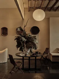 A warm and inviting dining room with a large table surrounded by chairs, a smaller table, and a vase with leaves as a centerpiece, featuring wood elements and a cozy atmosphere
