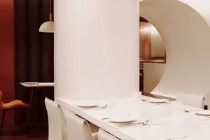 A dining area in a restaurant with a white table set with fine china, wine glasses, and various tableware, creating a sophisticated atmosphere