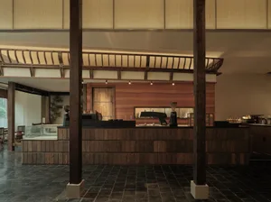 A warm and inviting restaurant interior with wooden walls and floors, featuring tables, chairs, and potted plants, creating a cozy atmosphere