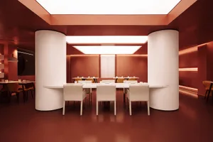 A modern dining area with a long wooden table and white chairs, surrounded by a red accent wall in a clean and neutral space