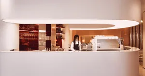 A casual bar scene with a woman standing behind a wooden counter, surrounded by bottles and cups, creating a welcoming atmosphere for customers