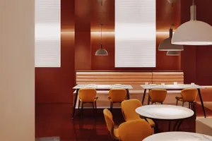 A restaurant interior with red walls, wooden floors, and dining tables with white tablecloths, creating a cozy atmosphere with various chairs and warm tones
