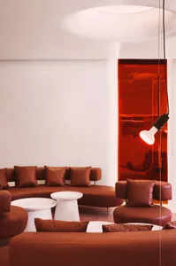 A modern living area with brown leather chairs and couches arranged around a coffee table, surrounded by red walls and white accents