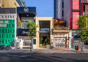 熱鬧的都市街景，包含數棟建築，其中一棟有寫著 Morico 的招牌，以及兩盆盆栽，一盆在中央附近，一盆在右側