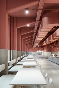 A spacious restaurant with a long dining table and multiple chairs, featuring a pinkish hue and a focus on functionality and comfort