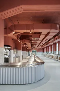 Industrial kitchen with a metal countertop island, various appliances, and chairs for staff to sit, with a clean and organized atmosphere
