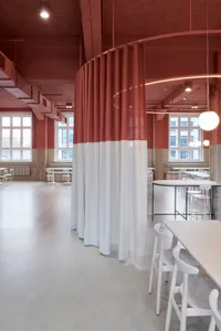 Modern restaurant interior with red and white walls, multiple dining tables, and chairs, featuring clean lines and minimalistic design elements