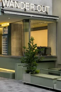 A cozy cafe with a counter, chairs, and potted plants, featuring bottles on display and a welcoming atmosphere