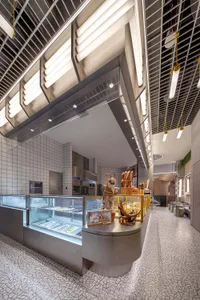 A modern restaurant interior with a kitchen area and dining space, featuring a large window, clean lines, and minimal decoration