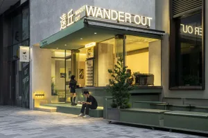 Modern Asian restaurant with green walls, glass front, and outdoor seating area with potted plants and a chair