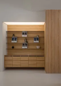 A wooden bookshelf with a brown finish, placed in a room with a white wall, holding neatly arranged books