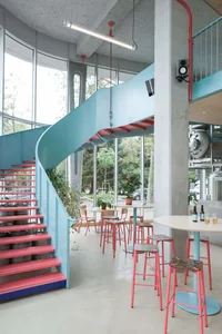 Modern living area with a spiral staircase, dining table, potted plants, and decorative bottles, featuring a mix of red and blue hues