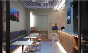 Empty restaurant interior with modern design, white walls, and dim lighting, featuring several tables and chairs in a spacious dining area