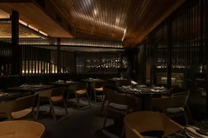 A modern restaurant with wooden floors and walls, featuring dining tables and chairs in a welcoming atmosphere