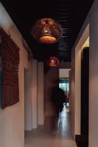 A dimly lit hallway with white walls, a black door, and two hanging lamps casting shadows on the floor and walls