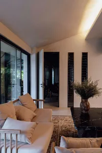 Open modern living area with a couch, chairs, and glass door leading to a patio, surrounded by white walls and a black countertop, with natural light from the glass door